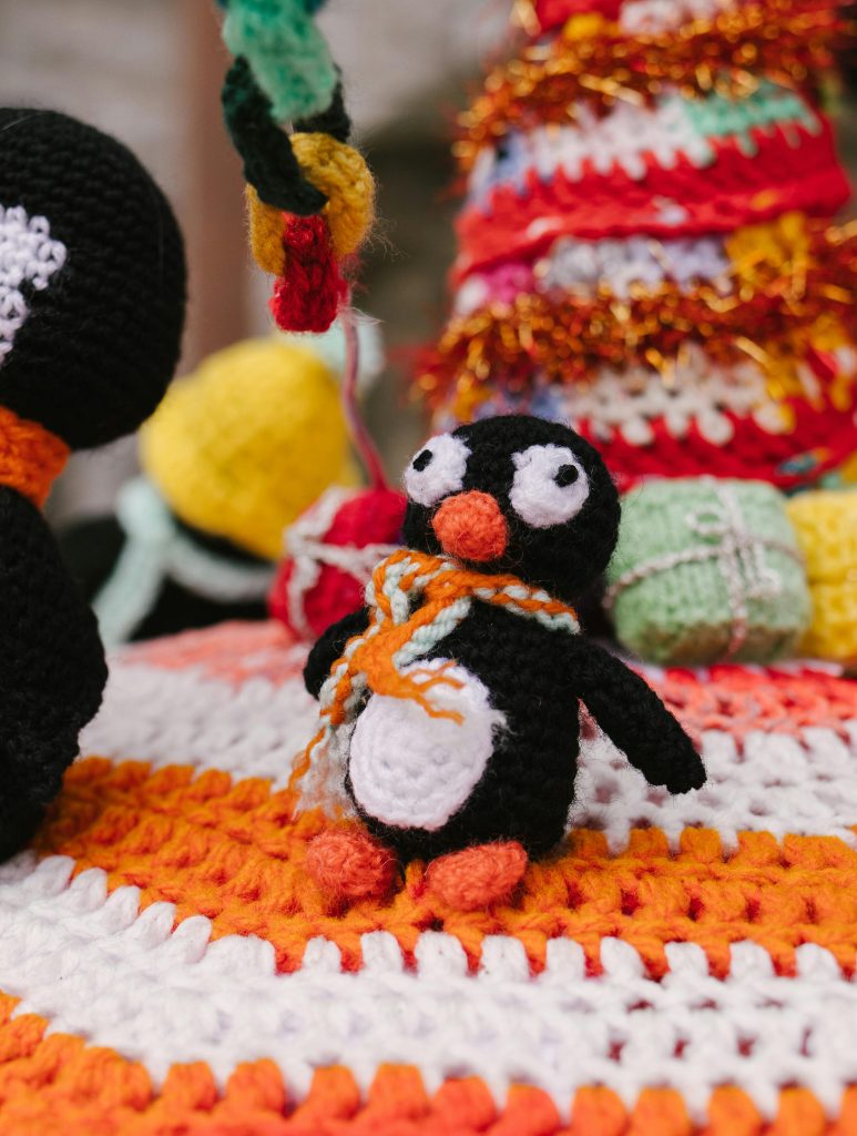 Close-up of a cute handmade crochet penguin toy with colorful crafts in the background.