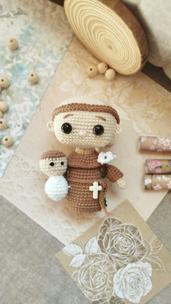Cute Saint Anthony amigurumi crochet doll with accessories on decorative surface.